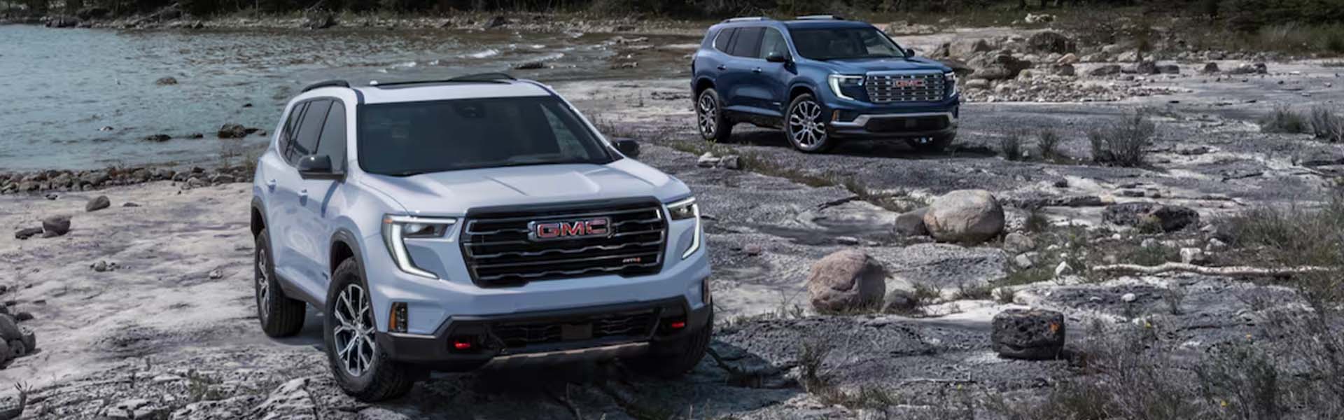 GMC SUVs parked on rocky lakeside terrain.