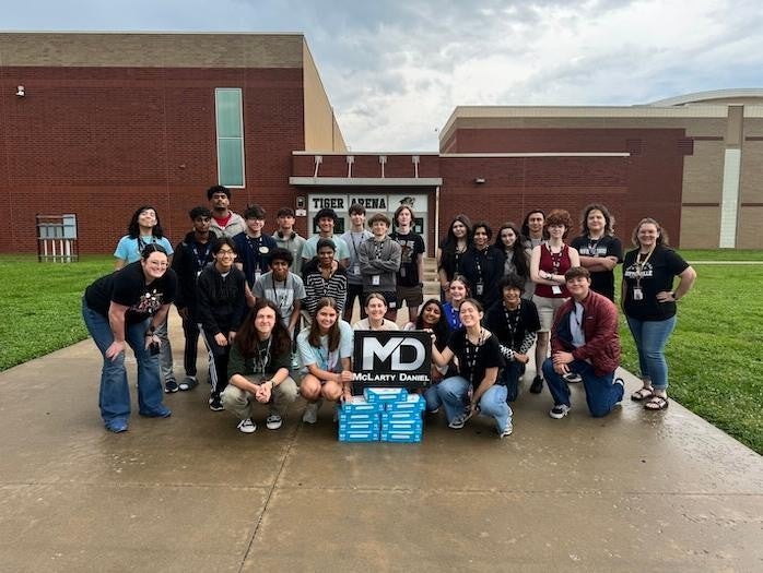 Group of students from debate team holding McLarty Daniel sign in front of Fayetteville High School