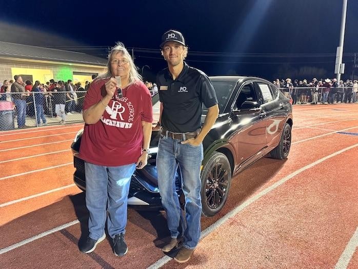 Paula Benson stands beside a dealership employee in front of her newly gifted Envista, smiling with appreciation for the recognition of her years of dedication to the Pea Ridge School District.