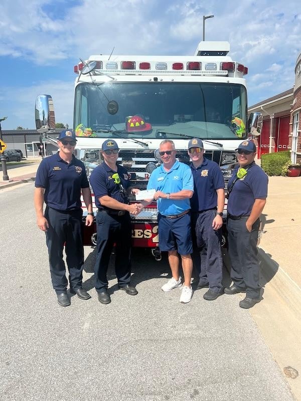 McLarty Daniel PR employee with fire department presenting check in front of fire truck