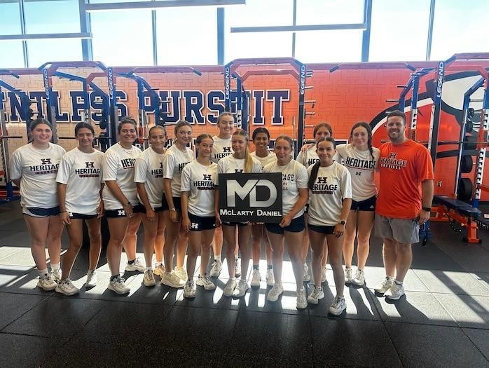 Girls from the Heritage softball team with coach holding McLarty Daniel sign in gym